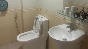 A bathroom with a toilet, sink, and a glass shelf with toiletries. - Tung Duong Motel HN -BAYLUXURY (Hanoi)