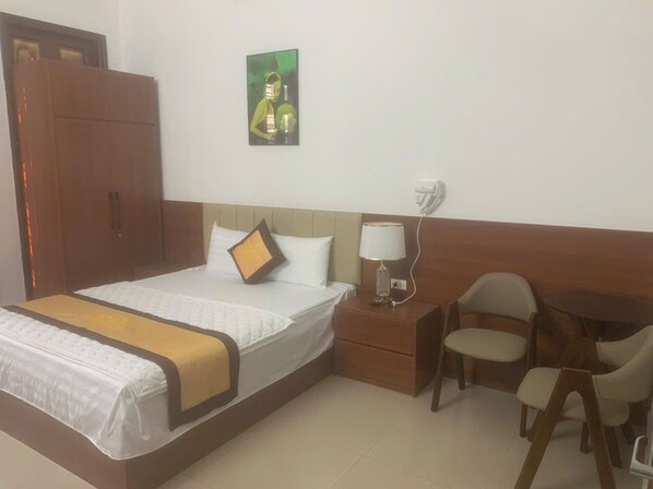Una habitación de hotel con una cama grande, una mesita de noche con lámpara, una silla y una pequeña mesa.