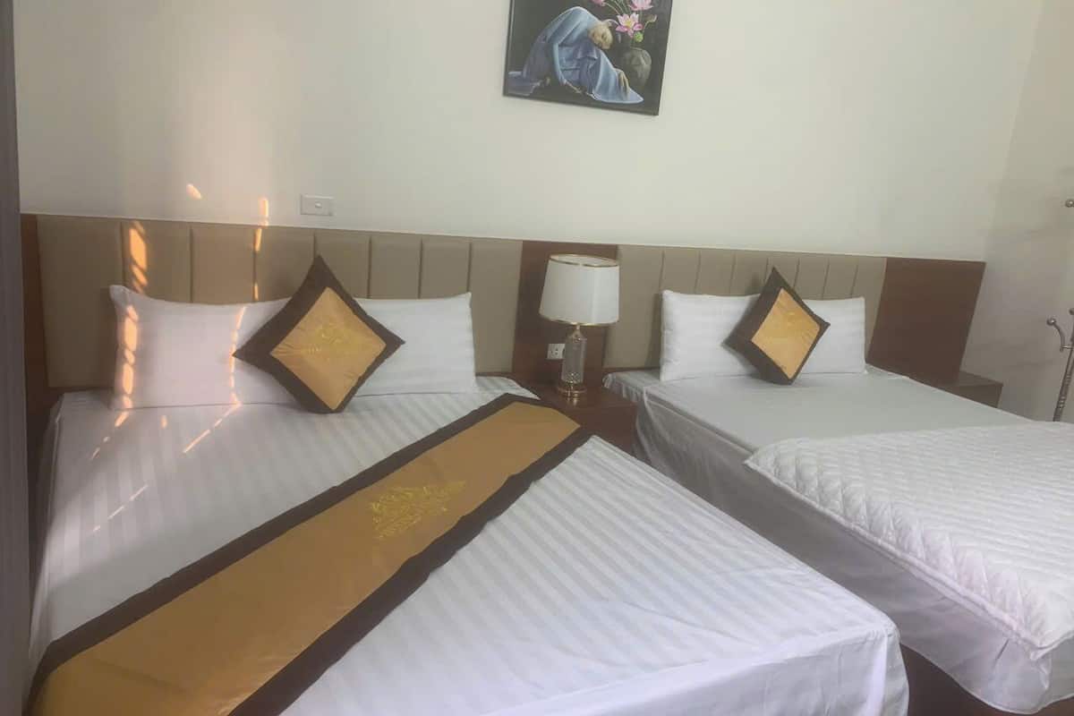 A hotel room with two beds, each with white bedding and a brown runner. There is a nightstand with a lamp and a wall-mounted painting above the beds.