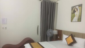 A hotel room with a bed, a desk, a chair, a fan, and a painting on the wall. - Tung Duong Motel HN -BAYLUXURY (Hanoi)