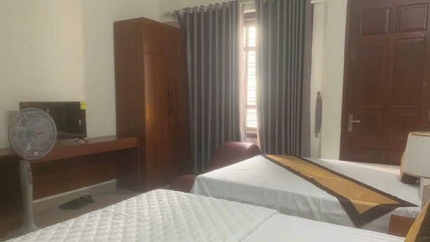 A hotel room with two beds, a desk with a computer, a wardrobe, and a window with curtains. - Tung Duong Motel HN -BAYLUXURY (Hanoi)