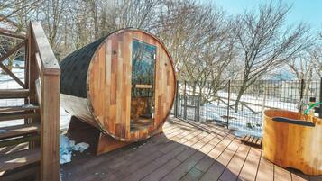 A wooden barrel-shaped structure with a glass door, a wooden deck, and a metal fence in the background.