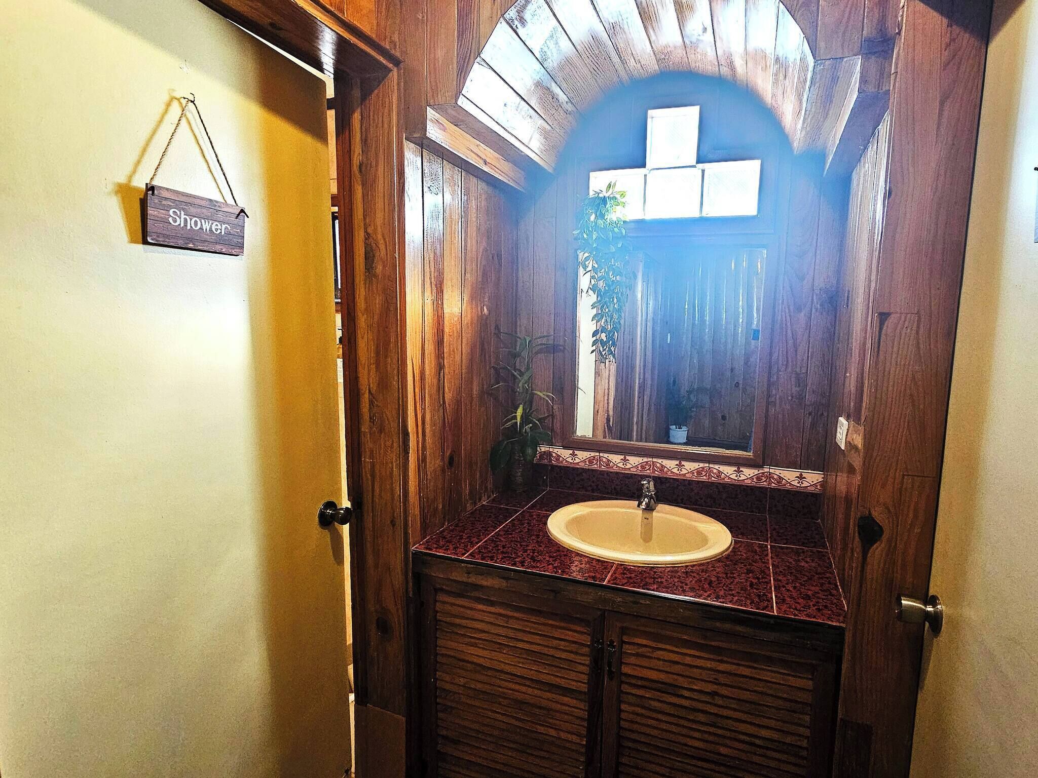 A wooden bathroom with a sink, mirror, and shower sign.