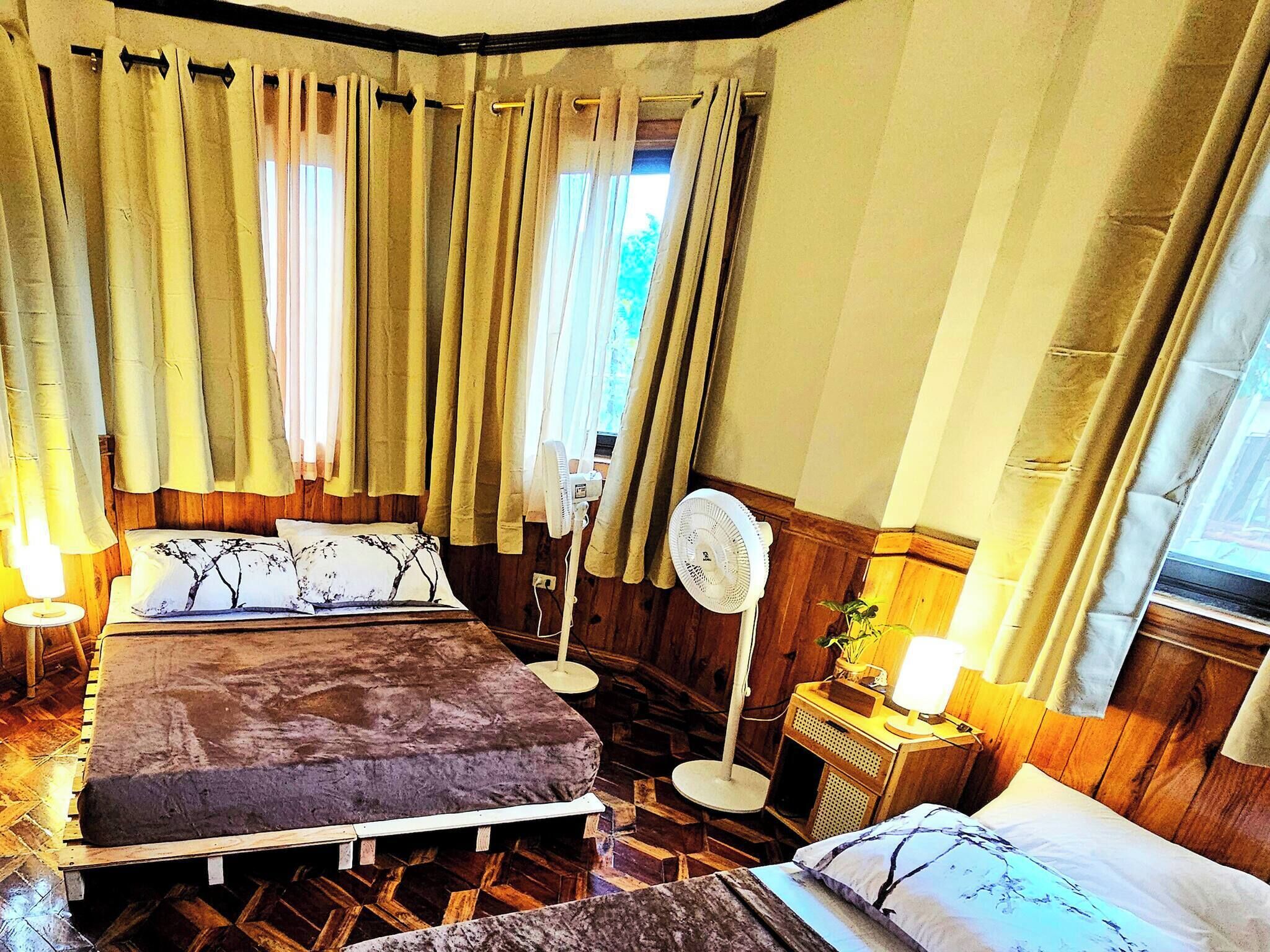 Une chambre à coucher avec un lit, une table de chevet, une lampe et un ventilateur sur pied.