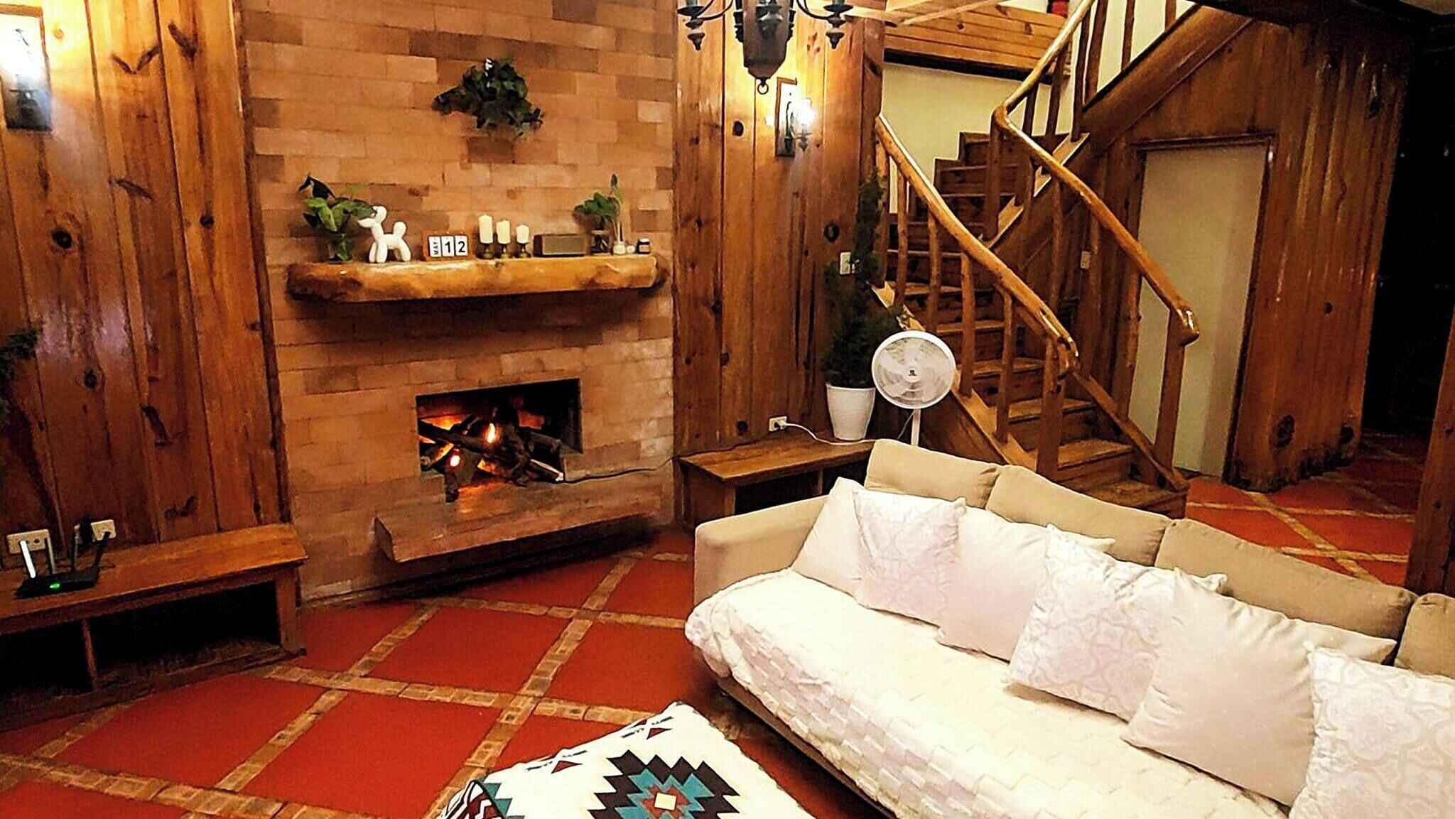 A cozy living room with a fireplace, wooden walls, a sofa, and a staircase.