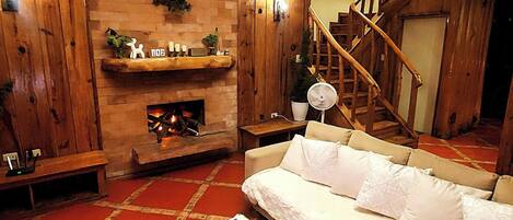 A cozy living room with a fireplace, wooden walls, a sofa, and a staircase.