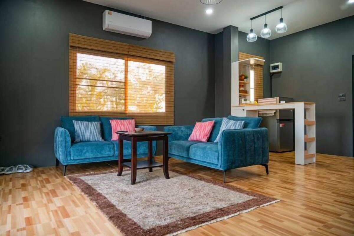 A modern living room with a blue sofa, a small wooden table, a rug, and a window with blinds.