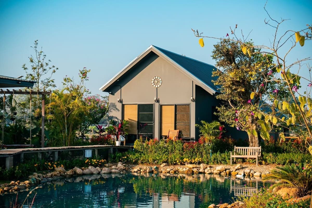 A modern house with a large window, a pool, and a garden with various plants and a bench.