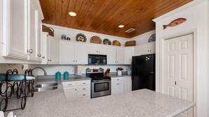 A kitchen with white cabinets, a granite countertop, a stainless steel sink, a black refrigerator, and a wooden ceiling.