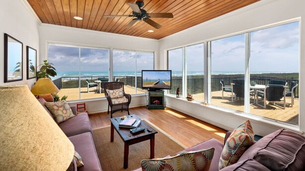 A spacious living room with a large TV, comfortable seating, and a balcony with ocean views.