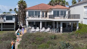 A two-story house with a balcony, a covered patio with chairs, and a pathway leading to the house.