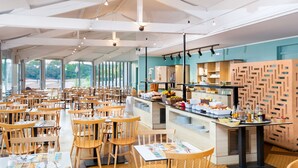 A spacious restaurant with high ceilings, wooden tables and chairs, a buffet counter with various food items, and large windows offering a view of the outdoors. - Sowell Family Pignada Plage by Interhome (Soustons)