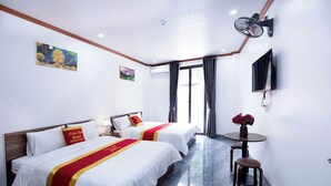 Une chambre d’hôtel avec deux lits, une télévision, la climatisation et une petite table sur laquelle est posé un vase de fleurs.