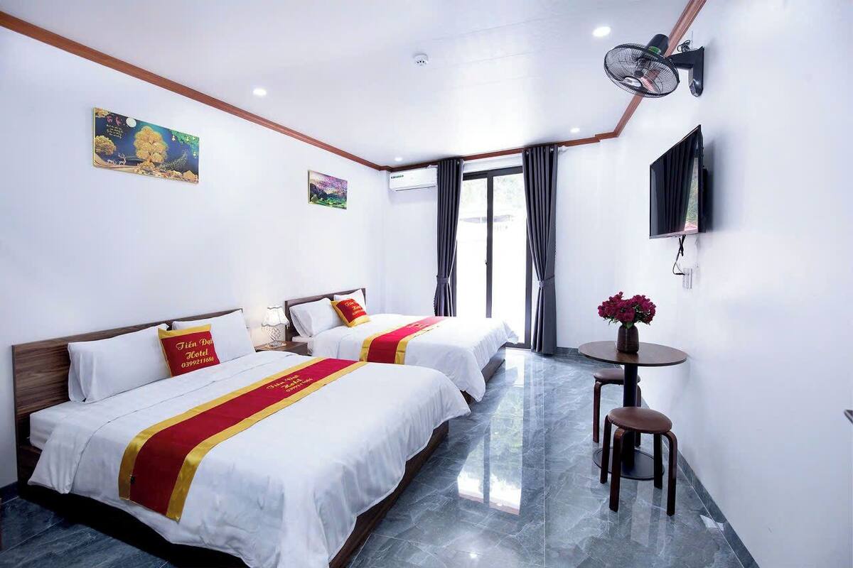 Una habitación de hotel con dos camas, un televisor, aire acondicionado y una pequeña mesa con un jarrón de flores.