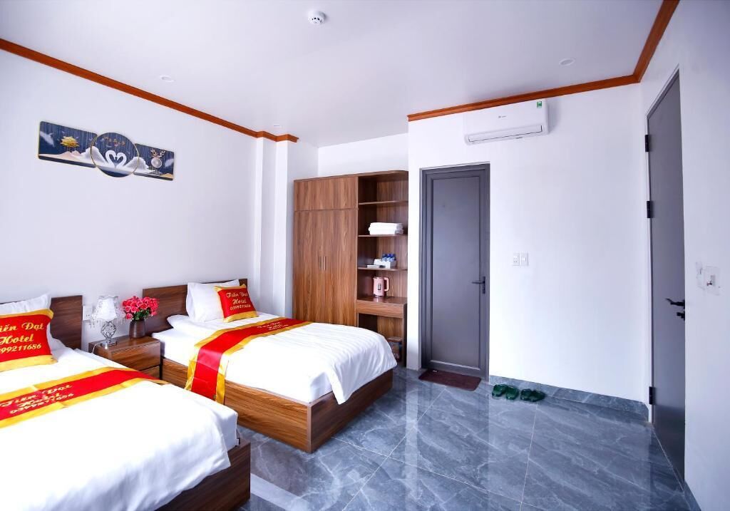 A hotel room with two beds, a wardrobe, a bedside table with a lamp, and a door.