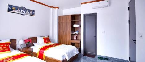 A hotel room with two beds, a wardrobe, a bedside table with a lamp, and a door.