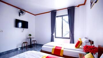 Une chambre d’hôtel avec deux lits, une télévision, une petite table avec une plante et une fenêtre avec des rideaux.