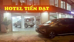 L’entrée d’un hôtel, avec une enseigne indiquant « HÔTEL TIÊN DAT » et plusieurs voitures garées.