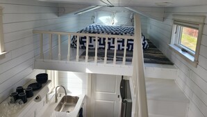 A compact, single-level room with a bunk bed, a small kitchenette with a sink and a window, and a view of the outdoors.