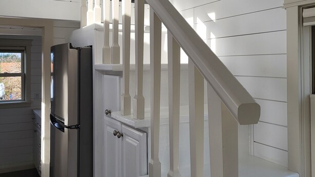 A staircase with white railings and a view of a kitchen area with a refrigerator.