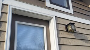 A house with a garage door, a window, and a wall-mounted light fixture.