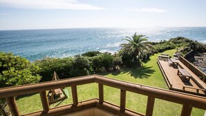 A balcony with a view of the ocean, a grassy area, and a wooden deck with picnic tables. - Tteuribada Pension (Seogwipo)