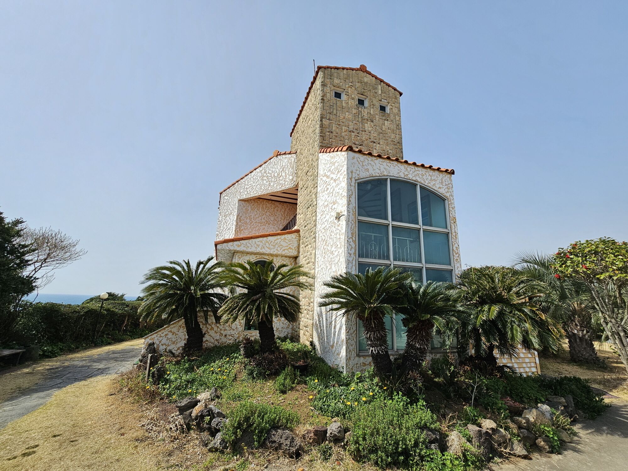 Un edificio de piedra con una torre, ventanas amplias y rodeado de palmeras y vegetación.