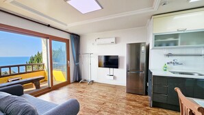 A modern room with a balcony, a flat-screen TV, a stainless steel refrigerator, and a kitchen area. - Tteuribada Pension (Seogwipo)