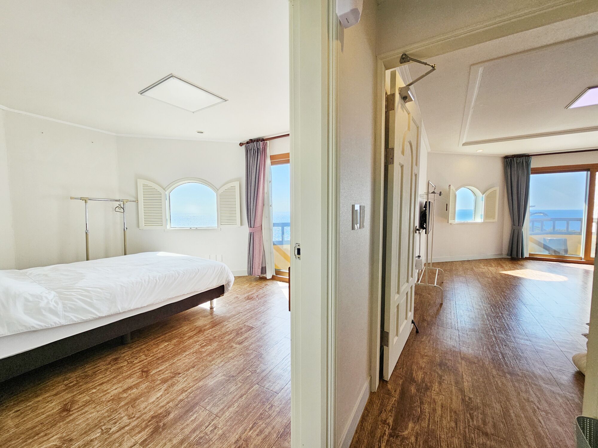 A bedroom with a bed, wooden flooring, a window with shutters, and a view of the sea.