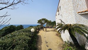 A pathway leading to a building with a white exterior and a view of the sea. - Tteuribada Pension (Seogwipo)