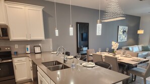 A modern kitchen with a large island, built-in appliances, and a dining area with a chandelier. - Florida Luxe Condo & Resort (Kissimmee)