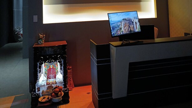 A reception desk with a monitor displaying a scenic view, a chandelier, and a wall sign for Hotel Japan Luna. - Japan Luna Hotel Binh Duong -BAYLUXURY (Ho Chi Minh City)