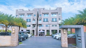 A multi-story hotel with a central entrance, parking area, and surrounding palm trees. - Aqua rooftop (Wujie)