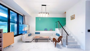 A modern living room with a white sofa, a coffee table, and a brown leather chair. There is a staircase with a glass railing leading to a balcony. - Aqua rooftop (Wujie)