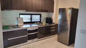 A modern kitchen with dark wood cabinets, a stainless steel refrigerator, a built-in oven, and a window above the sink. - Aqua rooftop (Wujie)