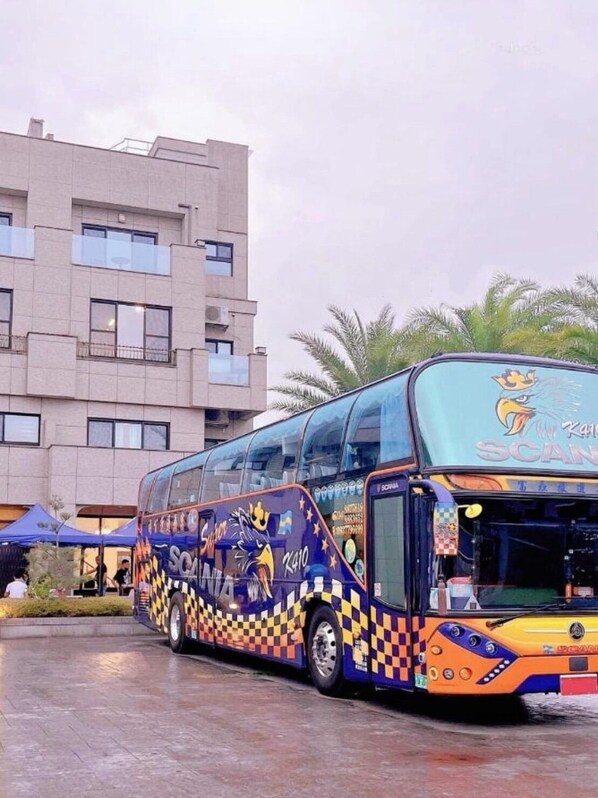 A colorful bus with a checkered pattern and a kangaroo logo parked in front of a building with multiple windows and palm trees. - Aqua rooftop (Wujie)