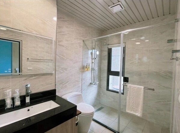A modern bathroom with a glass-enclosed shower, a white toilet, and a black countertop with a mirror.