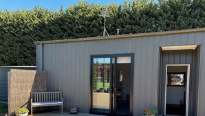 A modern building with a wooden deck, a bench, and a door leading to a covered outdoor area.