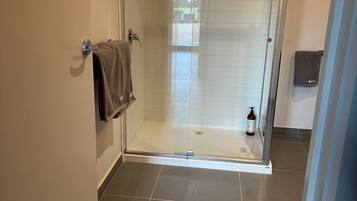A modern bathroom with a glass-enclosed shower, a towel rack, and a bottle of shampoo.