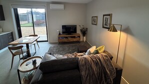 A modern living room with a sofa, TV, dining table, and a sliding glass door leading to a patio.