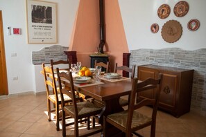 Un comedor con una mesa de madera, sillas y una estufa. Hay platos, vasos y un frutero sobre la mesa.