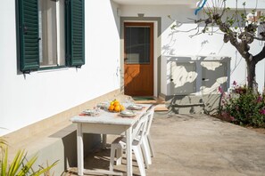 A white building with a wooden door, a table with plates and oranges, and a tree with pink flowers. - Fico apartment with garden (Loculi)