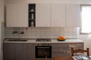 Una cocina con estufa a gas, horno, pileta y un cuenco con fruta sobre la encimera.