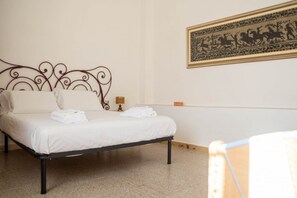 Una cama con estructura metálica, ropa de cama blanca y un cuadro colgado en la pared.