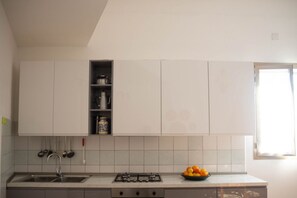Een keuken met witte kastjes, een gasfornuis, een spoelbak en een raam.