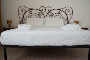 A neatly made bed with white linens, a metal headboard, and two bedside lamps on wooden nightstands. - Fico apartment with garden (Loculi)