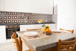 Une cuisine dotée d’un plan de travail en granit, de meubles blancs, d’un crédence à motifs, d’une cuisinière et d’une table à manger mise avec des assiettes et un vase rempli de citrons.