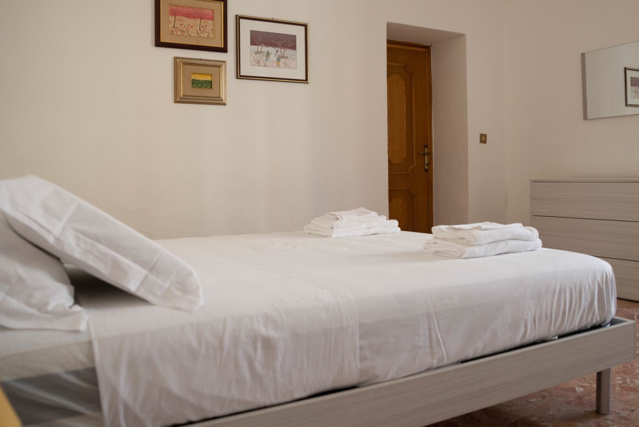 A neatly made bed with white linens, a wooden headboard, and a small bedside table with a white lamp.