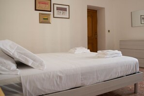 A neatly made bed with white linens, a wooden headboard, and a small bedside table with a white lamp. - Melograno apartment (Loculi)