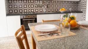 Une cuisine avec un mur recouvert de carreaux décoratifs, une table à manger avec des assiettes et des verres, et un panier rempli d’oranges.